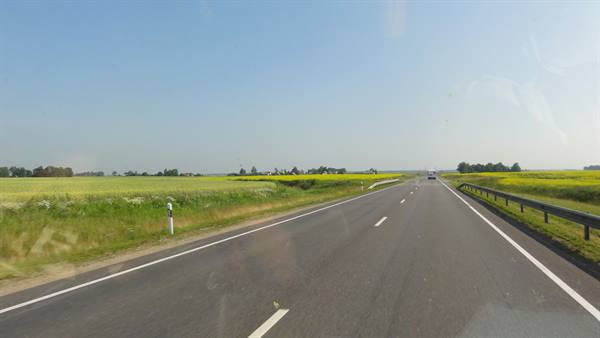 Straight highway cutting through yellow rapeseed fields under blue sky