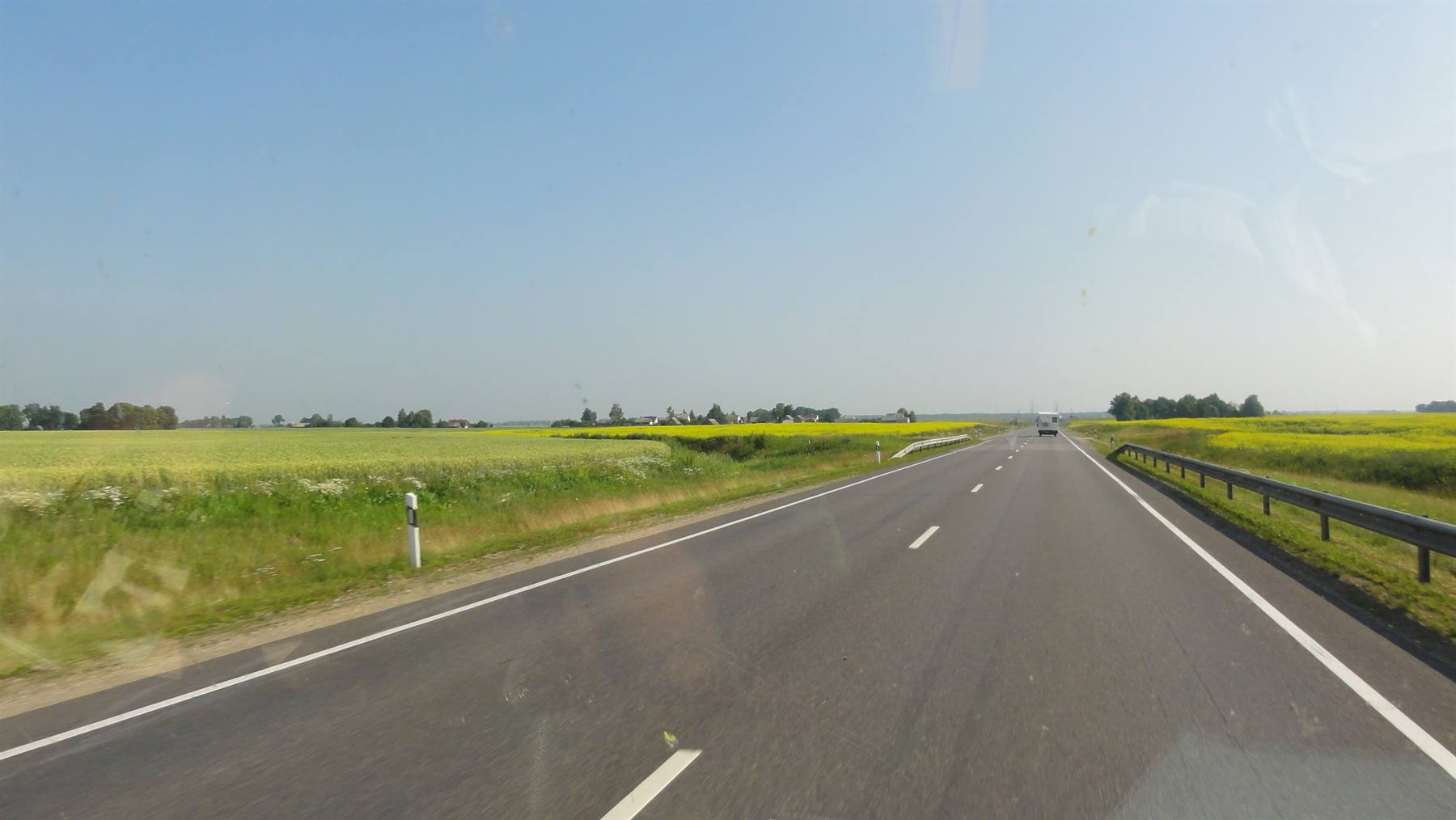 Autostrada diritta tra campi di colza gialli sotto cielo azzurro