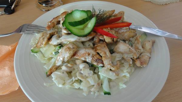 White plate with grilled chicken salad, cabbage, cucumber and pepper, on wooden table
