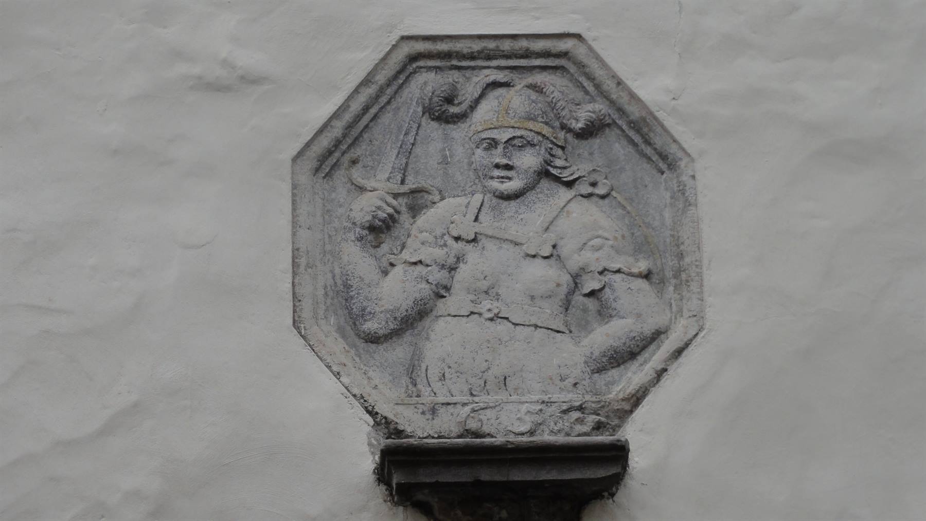 Bassorilievo ottagonale in pietra di guerriero con spada, su muro bianco