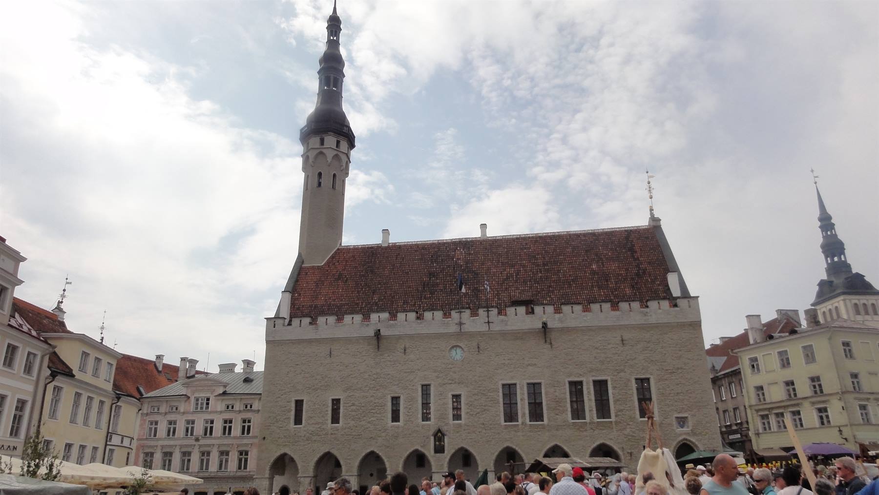 Municipio gotico di Tallinn con alto tetto di tegole, follda mercato sotto il cielo nuvoloso