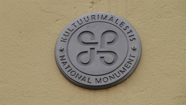 Grey metal plaque reading Kultuurimälestis National Monument on a yellow wall