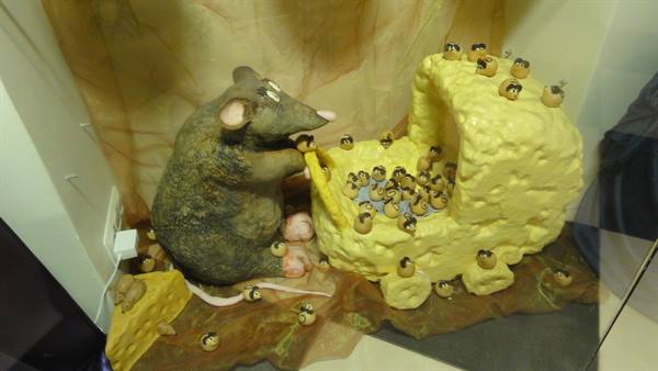 Sculpture of giant rat eating cheese surrounded by tiny mice
