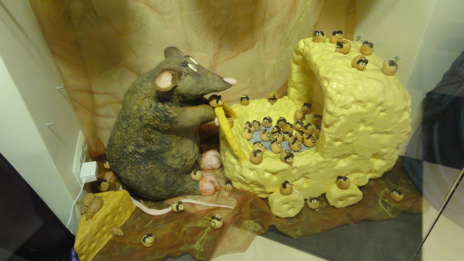 Scultura di topo gigante che mangia formaggio con topolini intorno