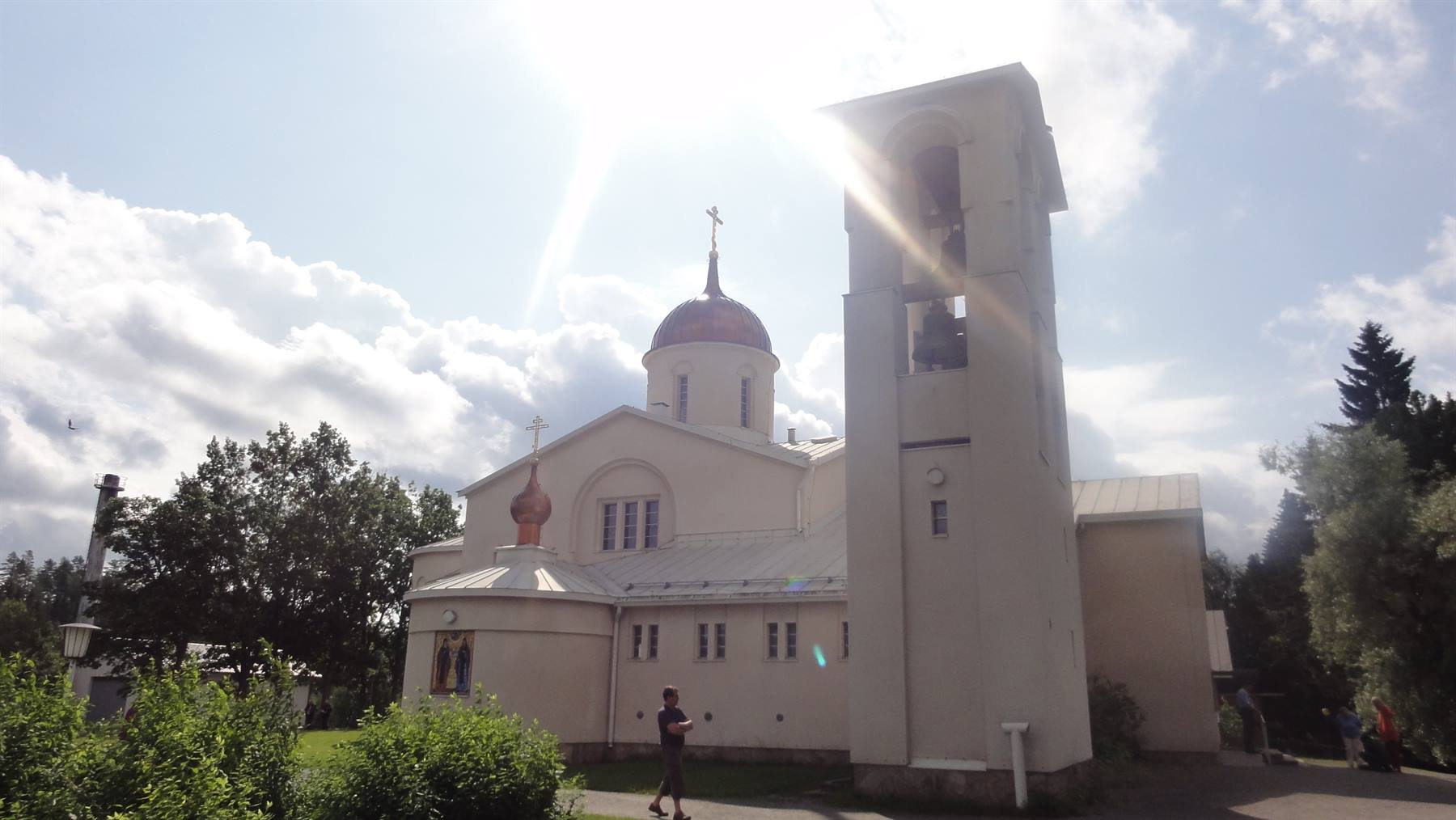 Chiesa ortodossa bianca con cupola di rame e campanile, un uomo cammina sotto il sole
