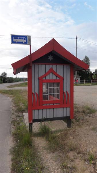 Red and grey wooden bus stop shelter beside a rural road