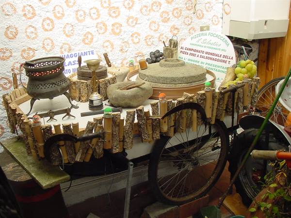 Cart decorated with wooden logs, old stone mill and brazier, near pizzeria sign