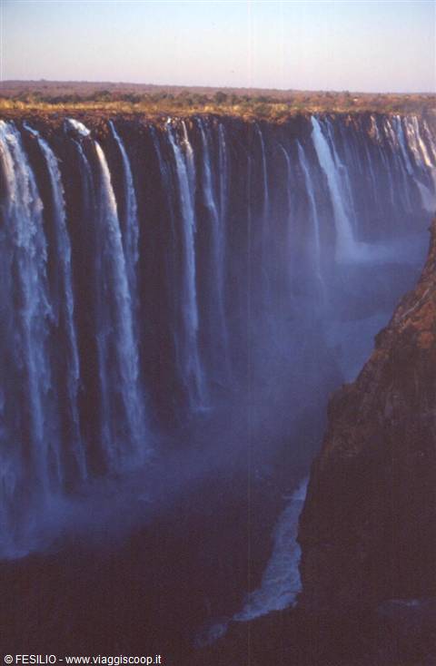 Victoria Falls: curtain of water over basalt cliff, mist in gorge