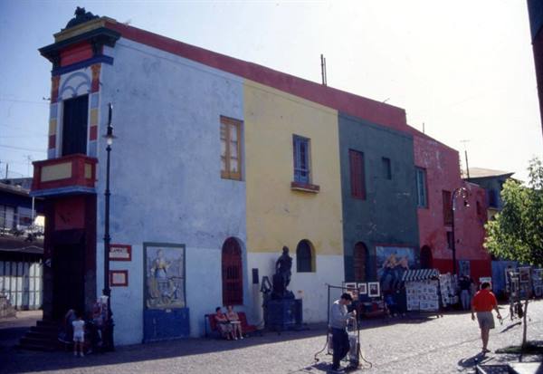 Colorful painted houses on Caminito street, painters and tourists in bright sunlight