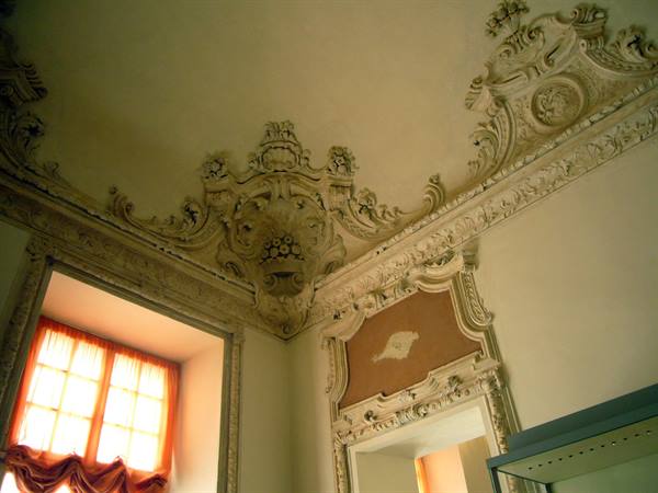 Baroque stucco ceiling above a doorway, light through a curtained window
