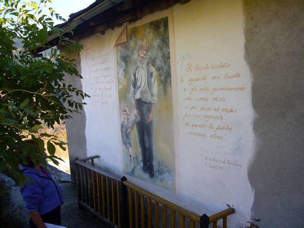 Mural on a house wall: elderly man with child beside painted verses, woman watching