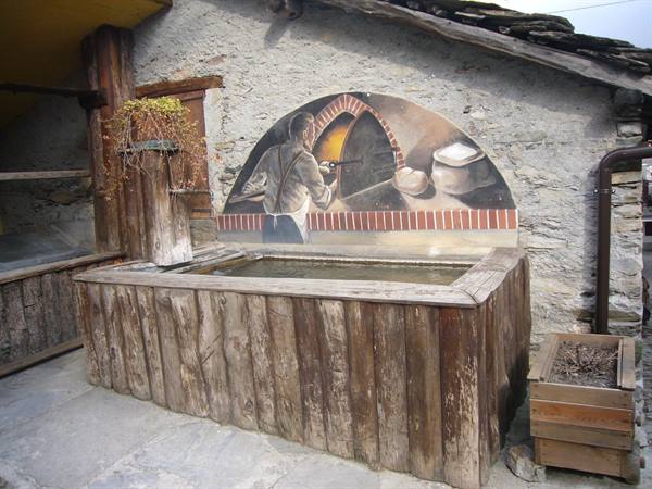 Wooden trough in front of a painted bread oven mural on stone wall