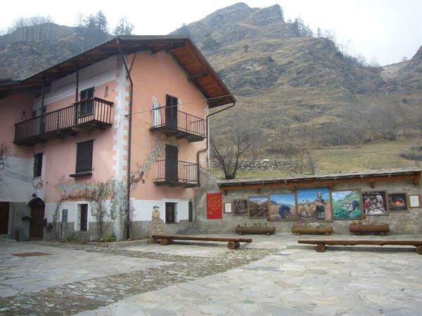 Pink frescoed house with wooden benches on stone courtyard, mountain rising behind