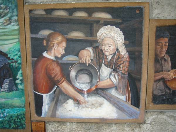 Wall painting: two women in traditional dress knead dough, pouring water from a pot