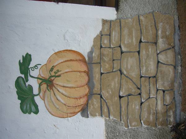 Painted pumpkin with green leaves on white wall beside faux stones