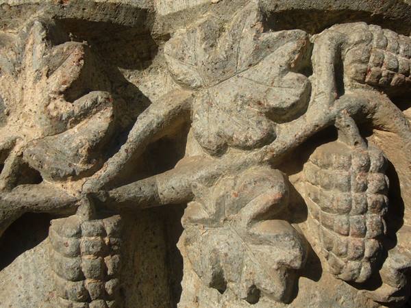 Carved stone grape clusters and leaves in direct sunlight