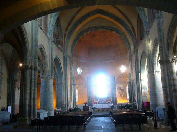 Illuminated apse inside Sacro Monte church, altar, stone columns and pews