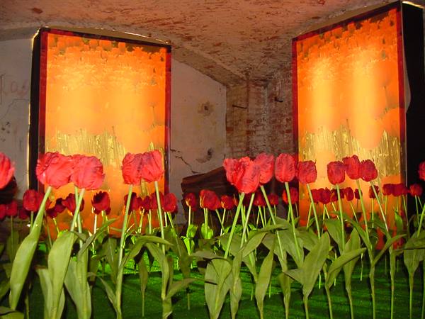 Red artificial tulips before lit orange panels, brick vaulted crypt