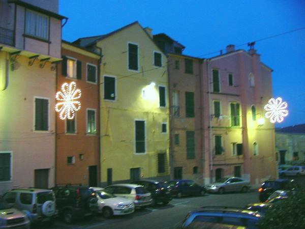 Colorful houses with flower-shaped lights over a square with parked cars at dusk