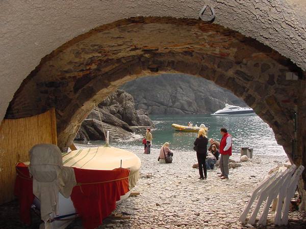 Covered boat under stone arch, people on San Fruttuoso pebble beach