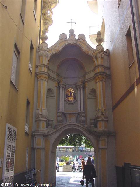 Baroque stone arch between yellow buildings, golden shrine, people walking through
