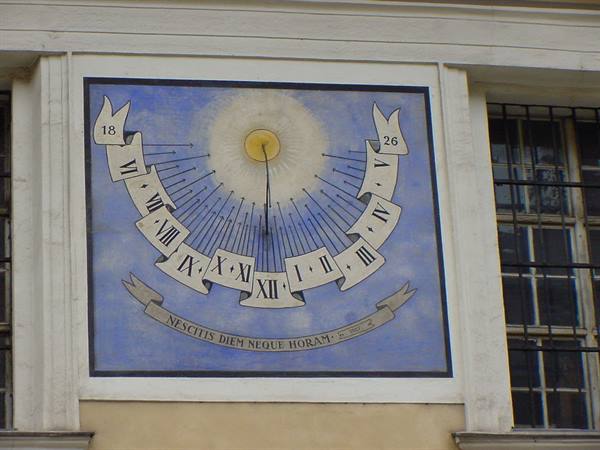 Painted sundial on a wall with golden sun, Roman numerals and Latin motto