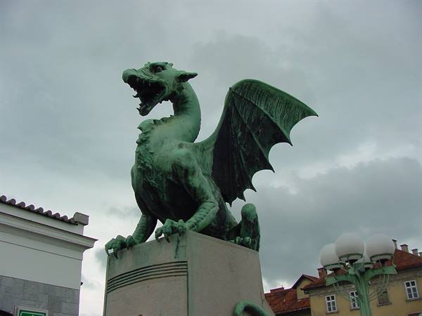 Bronze dragon statue on Ljubljana bridge, wings spread against cloudy sky