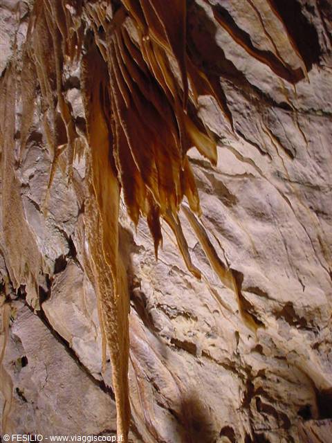 Orange limestone drapery and stalactite flowstone lit inside the cave