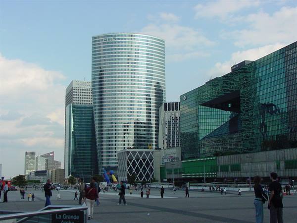 Visitors stroll across the La Défense esplanade among mirrored glass skyscrapers