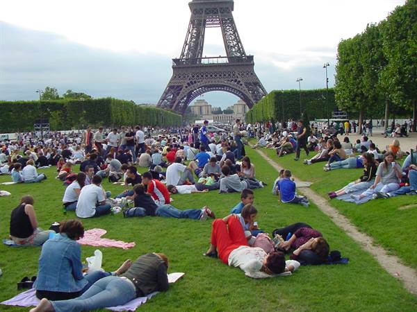Crowd of tourists relaxing on the Champ de Mars grass beneath the Eiffel Tower