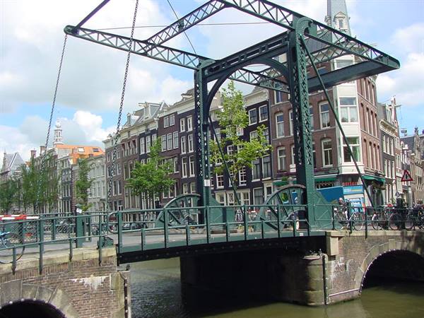 Green iron drawbridge over Amsterdam canal among brick canal houses