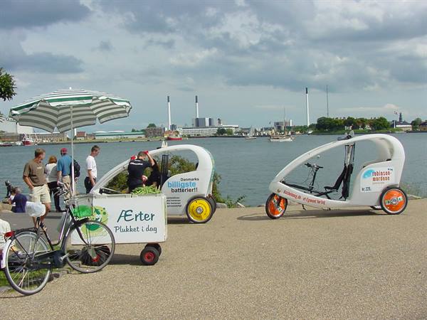 Advertising cargo trikes parked by the waterfront under a striped umbrella