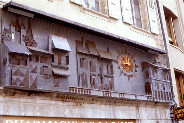 Metal sundial with sculpted houses on a pharmacy facade