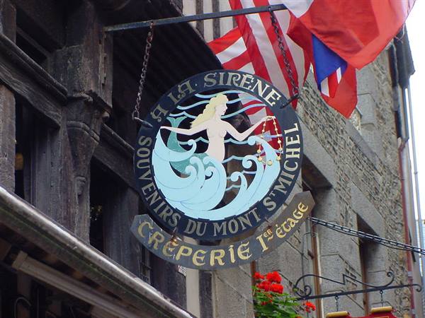 Mermaid sign for souvenirs and crêperie at Le Mont-Saint-Michel, flags hanging