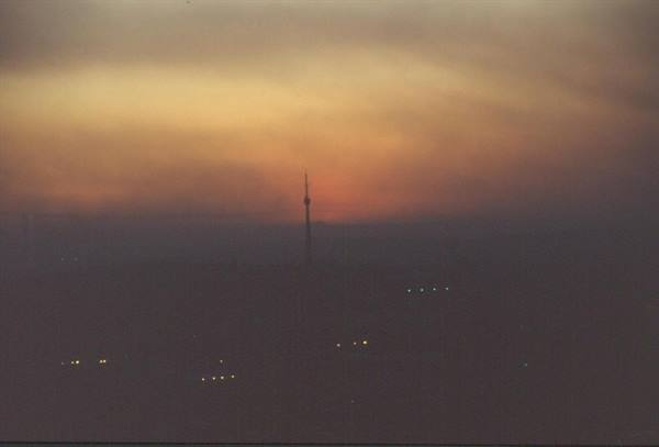 Radio tower silhouette in orange haze, city lights glowing below