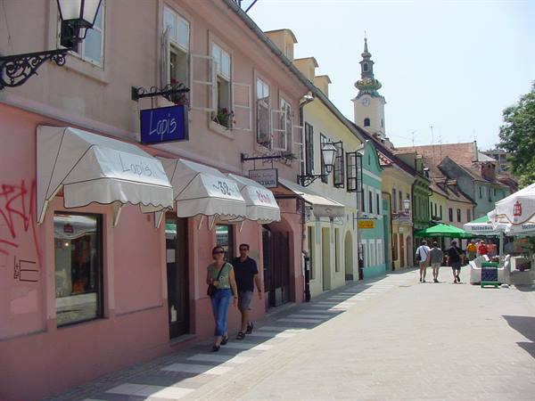 Pedestrians walking along colorful car-free street in Zagreb, church tower behind