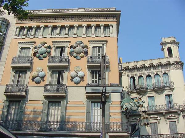 Modernist Barcelona facade with decorative umbrellas and dragon, under blue sky