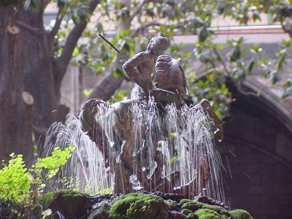 Bronze statue with spraying water, green moss, trees and stone arches