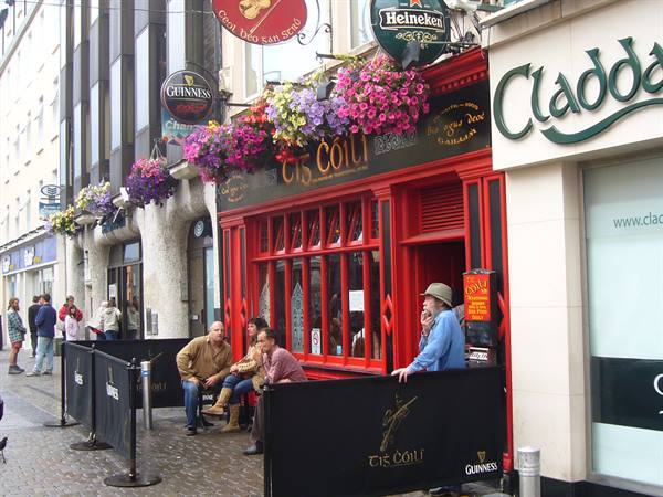 Tis Cóili red pub in Galway, hanging flowers, customers seated outside