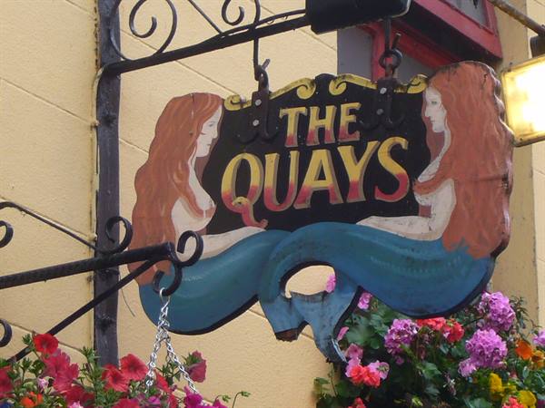Wooden painted pub sign with red-haired mermaids reading The Quays