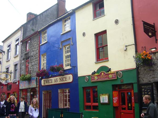People walk past brightly painted blue, cream and green shopfronts on a street
