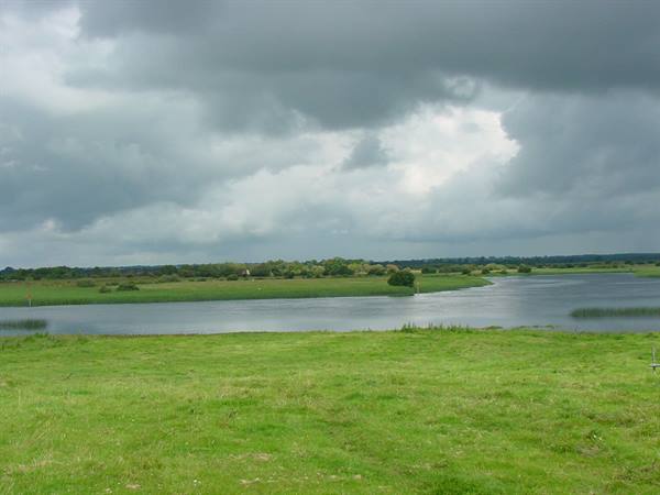 River winding between green meadows under grey storm clouds