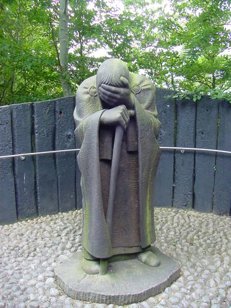 Stone statue of hooded figure covering its face, surrounded by trees