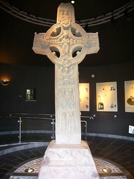 Carved stone Celtic high cross displayed inside a museum with dark walls