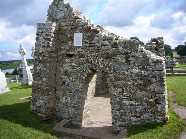 Stone church ruins with arched doorway among Celtic crosses in graveyard