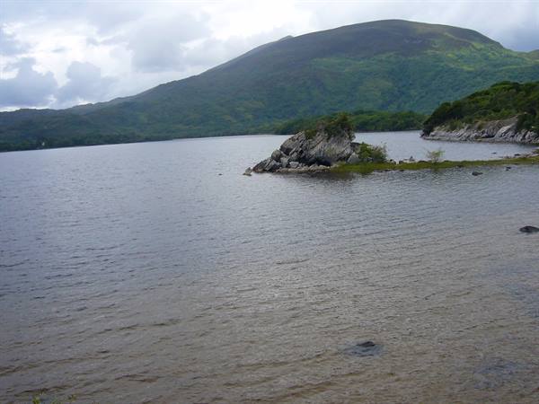 Rocky outcrop in Muckross Lake, green mountains and cloudy sky at Killarney