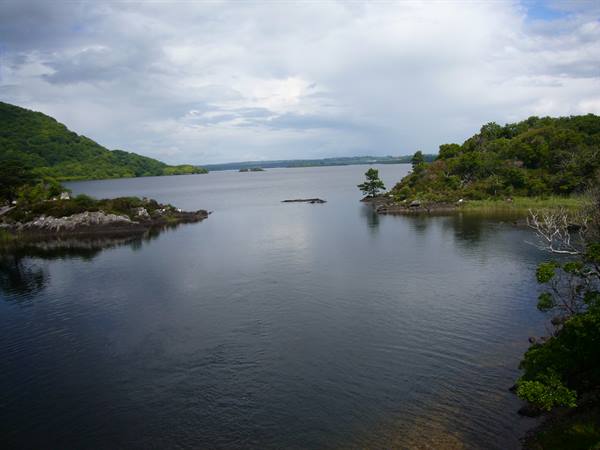 Killarney lake: dark water between green hills and rocky islets, cloudy sky