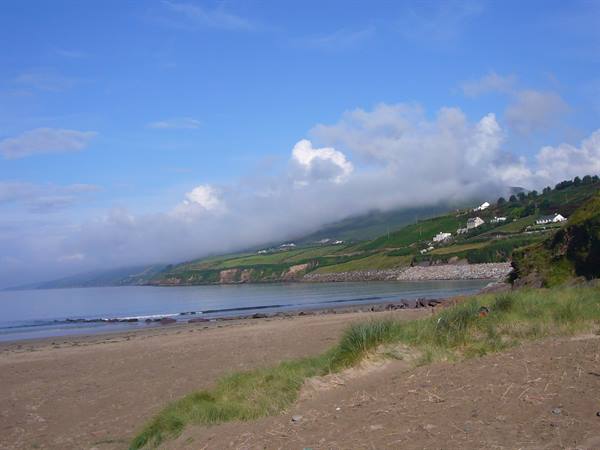 Sandy beach with dune grass, white houses on green hills and low clouds