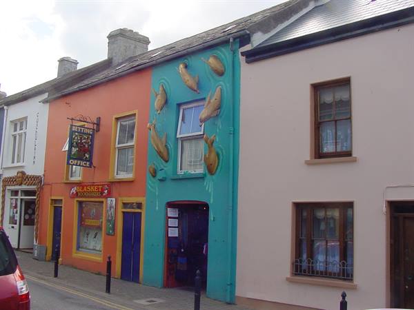 Turquoise facade with painted dolphins beside colorful shops on the street