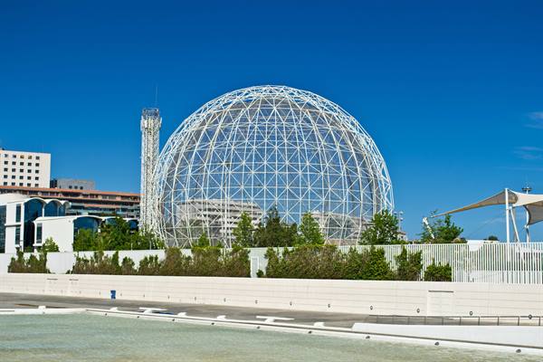 Giant steel lattice sphere in Seville, bright sunlight, white wall and hedges